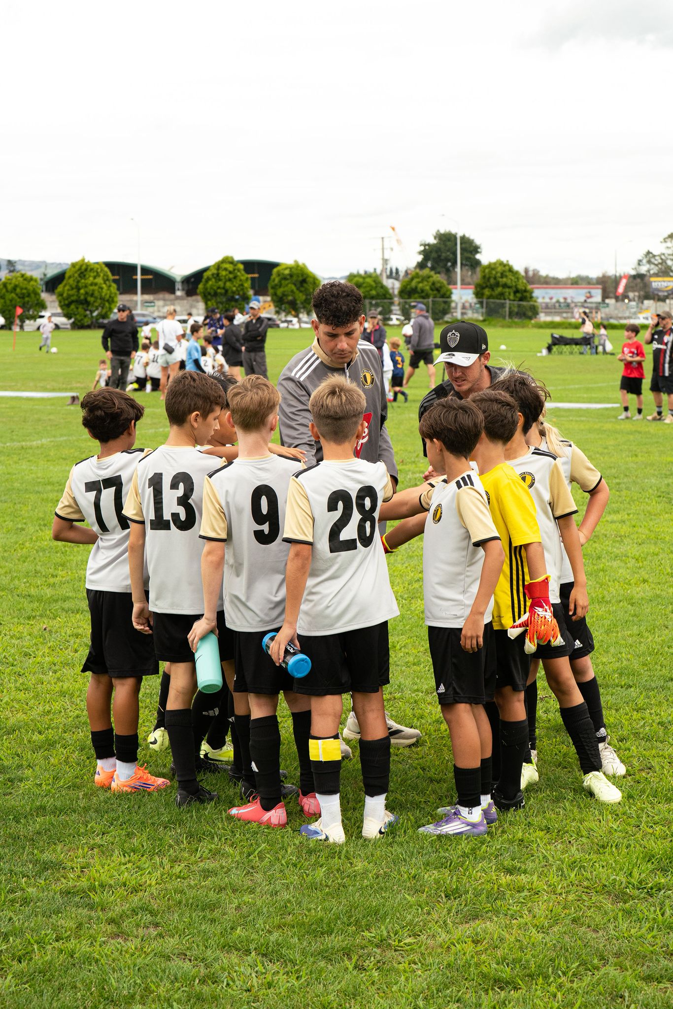 Only Ballers coaches giving a team talk to players in white and gold kits on the pitch