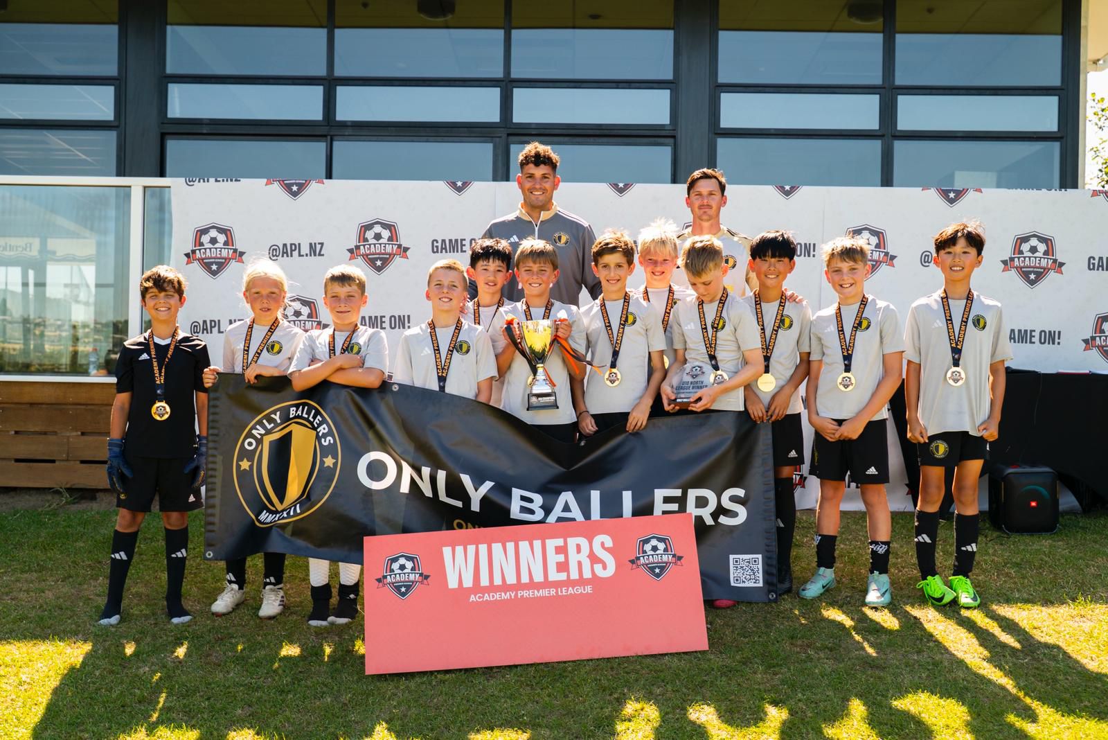 Only Ballers U10 team with coaches holding the winners banner, trophy, and medals at the APL ceremony