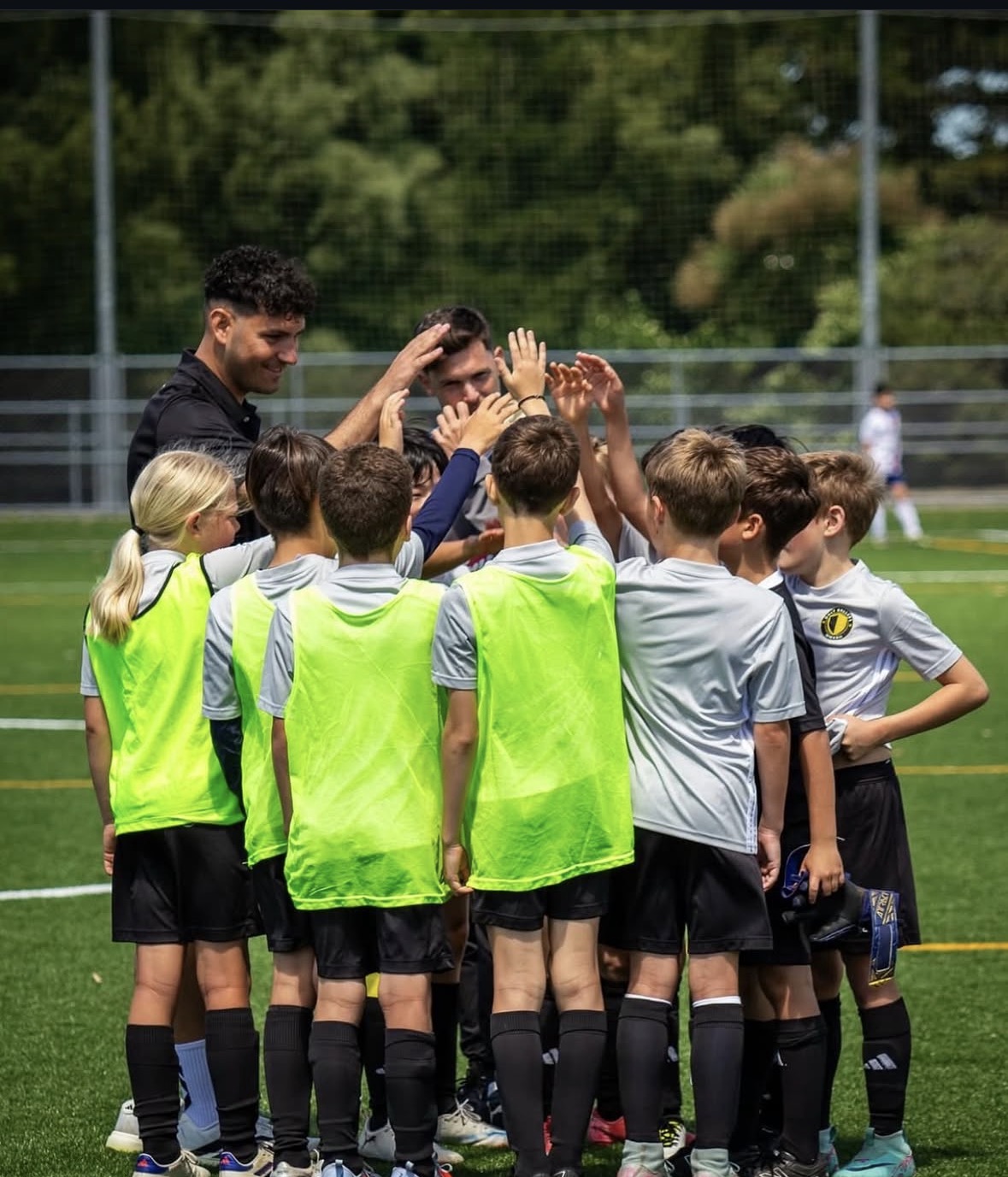 Coach leading a team huddle with young players raising hands together